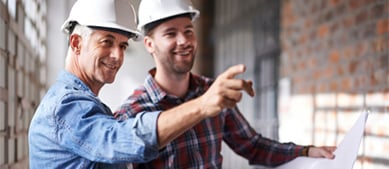 two men with hardhats looking at blueprints
