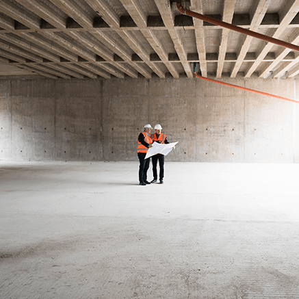 two people on construction site looking at blueprints